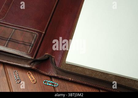 Un ricco raccoglitore in pelle è aperto, mostrando pagine vuote e graffette colorate nelle vicinanze. Foto Stock