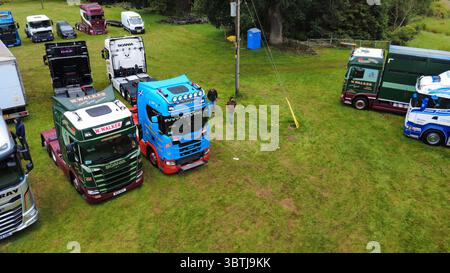 Vista aerea di una fila di veicoli industriali lucidati, compresi i modelli Scania, Volvo e DAF, parcheggiati su un campo erboso durante una fiera dei veicoli in Scozia Foto Stock