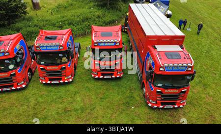 Vista aerea di una fila di veicoli industriali lucidati, compresi i modelli Scania, Volvo e DAF, parcheggiati su un campo erboso durante una fiera dei veicoli in Scozia Foto Stock