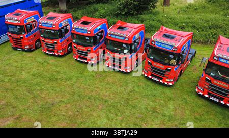 Vista aerea di una fila di veicoli industriali lucidati, compresi i modelli Scania, Volvo e DAF, parcheggiati su un campo erboso durante una fiera dei veicoli in Scozia Foto Stock