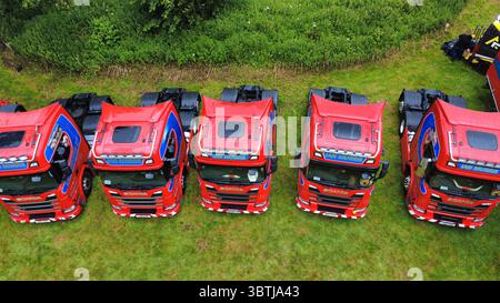 Vista aerea di una fila di veicoli industriali lucidati, compresi i modelli Scania, Volvo e DAF, parcheggiati su un campo erboso durante una fiera dei veicoli in Scozia Foto Stock