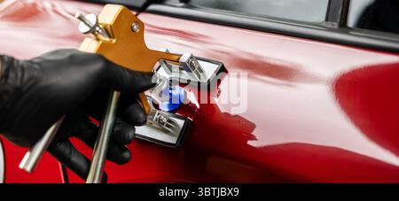 attrezzo di riparazione ammaccature per auto senza verniciatura. Uomo che fissa la portiera del veicolo danneggiata con tecnologia PDR Foto Stock