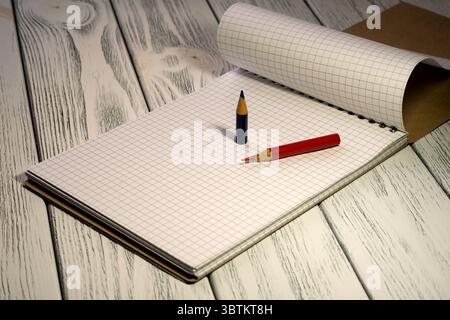 Blocco note vuoto aperto con carta a scacchi con matite colorate in cartoleria al crepuscolo Foto Stock