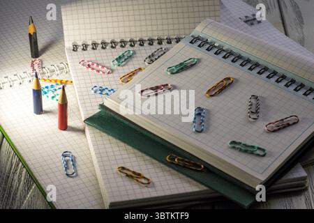 Blocchi appunti vuoti aperti con fogli sfusi a scacchi con matite e graffette in materiale cartaceo al crepuscolo Foto Stock
