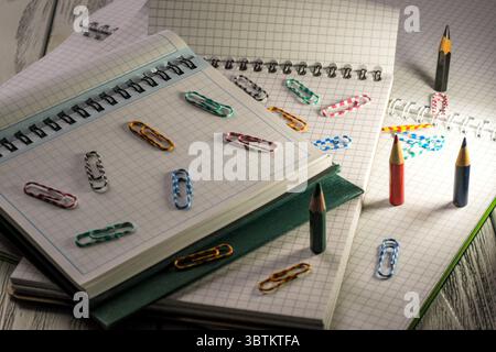 Blocchi appunti vuoti aperti con fogli sfusi a scacchi con matite e graffette in materiale cartaceo al crepuscolo Foto Stock