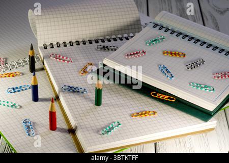 Blocchi appunti vuoti aperti con fogli sfusi a scacchi con matite e graffette in materiale cartaceo al crepuscolo Foto Stock