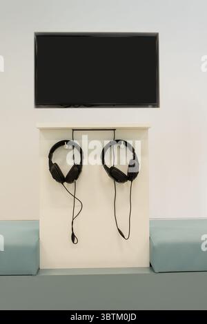 Un paio di cuffie moderne sono appese alla parete della sala di registrazione. Le cuffie sono appese alla parete. La TV è sul muro. Foto Stock