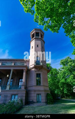 Primo piano della storica torre del castello di Biesdorf a Berlino, circondata da alberi lussureggianti e cielo estivo blu. Foto Stock