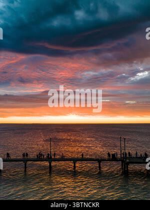 Vista aerea di un molo che si estende nell'oceano mentre il tramonto dipinge il cielo con vivaci tonalità arancio e rosa, Australia Occidentale, Australia Occidentale, Australia Occidentale, Australia. Foto Stock