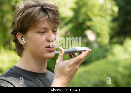 Giovane biondo caucasico che registra un messaggio vocale sul cellulare. All'aperto. Primo piano Foto Stock