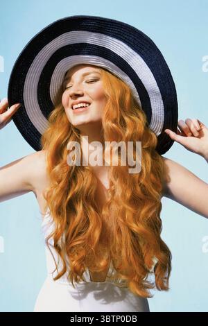 Ritratto di una giovane donna spensierata con lunghi capelli rossi ricci che indossano un cappello a righe Foto Stock