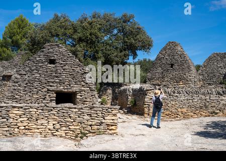 Turista che scatta fotografie con lo smartphone al le Village des Bories - edifici a secco del XVII secolo - a Gordes in Provenza Foto Stock