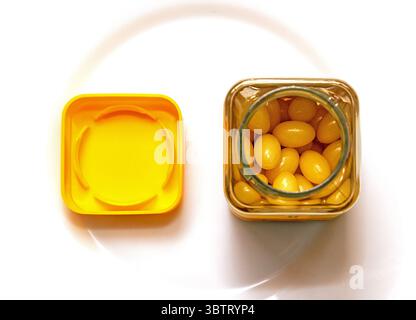 Aprire il flacone di plastica con gel in pillole gialle e il coperchio accanto a un contenitore Foto Stock