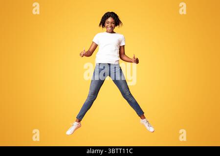 afroamericana gioiosa donna saltando e mostrando il pollice in su Foto Stock