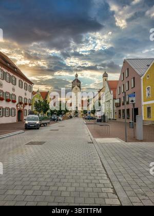Vista della strada principale con case storiche, la splendida torre ex porta della città di Erding, Germania, con il suggestivo cielo del tramonto Foto Stock