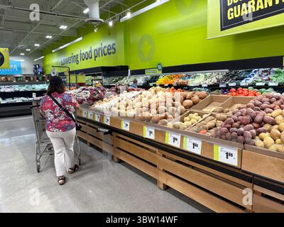 Cliente con carrello nella sezione prodotti del supermercato, con patate fresche e cipolle. Un segnale di "riduzione dei prezzi dei prodotti alimentari" mette in evidenza i consumatori a prezzi accessibili Foto Stock