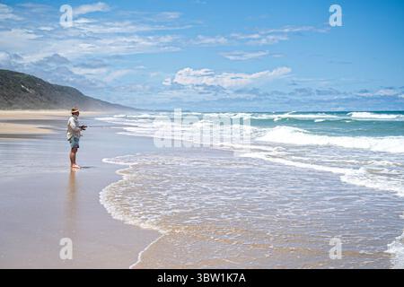 Pescatore solitario che pesca su un'ampia spiaggia sabbiosa. Teewah Beach, Great Sandy National Park, Queensland Australia Foto Stock