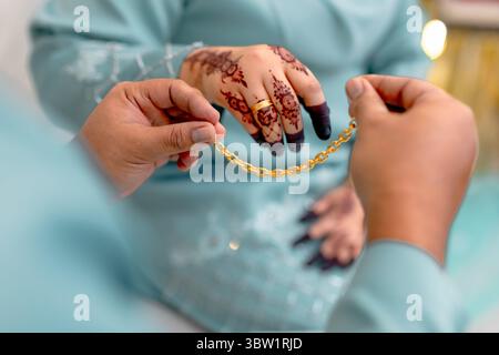 Uno sposo presenta una splendida catena d'oro alla sua sposa, un simbolo tradizionale di impegno e di amore duraturo nelle usanze matrimoniali malesi. Foto Stock