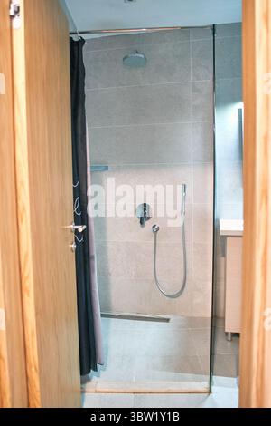 Cabina doccia moderna con porta in vetro, piastrelle grigie lucide e design minimalista in un elegante ambiente da bagno. Foto Stock