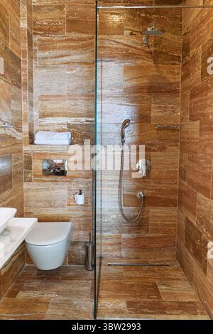 Un bagno elegante con piastrelle in travertino e box doccia in vetro che creano un'estetica moderna ed elegante con un design minimalista. Foto Stock