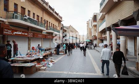 Folle di persone navigano in un vivace mercato di Baghdad, impegnandosi nello shopping e socializzando tra i venditori locali. Foto Stock