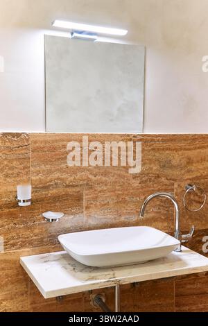 Un bagno contemporaneo con lavandino in marmo pulito, finiture eleganti e un decor elegante, impreziosito da luci soffuse e uno specchio riflettente per un lu Foto Stock
