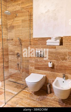 Un bagno contemporaneo con WC a parete, un'elegante doccia in vetro ed eleganti piastrelle marmoree marroni, che offrono un aspetto lussuoso e moderno. Foto Stock