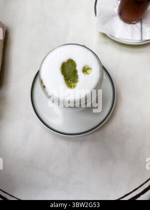 Un bicchiere trasparente di tè verde matcha nel caffè su un tavolo bianco. Foto di alta qualità Foto Stock