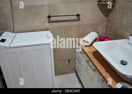 Una moderna lavanderia con lavatrice, lavandino, ripiano in legno e armadietto. lo spazio combina funzionalità e stile con il beige Foto Stock