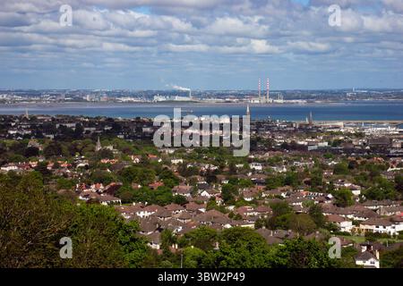 Ampia vista aerea di una vibrante città di Dublino con diversi tetti, vegetazione lussureggiante e un'ampia baia che si estende fino a colline lontane sotto un cielo luminoso Foto Stock