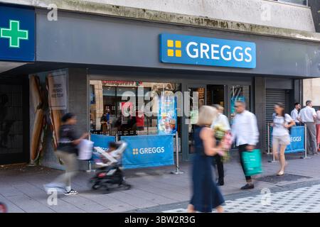 Greggs Bakery in Queen Street Cardiff con i pedoni sfocati in movimento che passano davanti Foto Stock