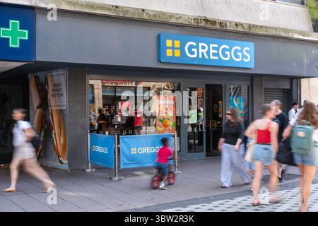 Greggs Bakery in Queen Street Cardiff con i pedoni sfocati in movimento che passano davanti Foto Stock
