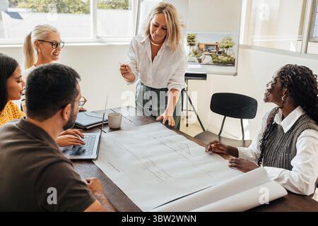 Team di architetti che discutono i piani di costruzione in un ufficio luminoso, che include quattro donne e un uomo di età diverse, riflettendo creatività, lavoro di squadra, AN Foto Stock