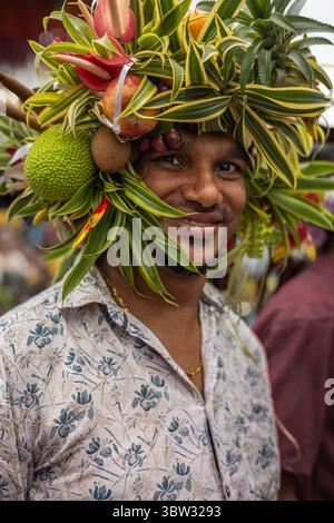 Parata del tradizionale carnevale di Goa. Festeggiamenti per il Carnevale. Il giovane si sta divertendo indossando una corona di frutta e fiori. Festa di Sao Joao Foto Stock