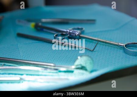 Una vista ravvicinata degli strumenti chirurgici che posano su un panno chirurgico color acqua in un ambiente medico, evidenziandone la precisione e il design per la chirurgia Foto Stock