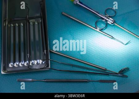 Vista ravvicinata degli strumenti chirurgici su un telo chirurgico blu con riflesso che evidenzia la loro superficie in acciaio e la levigatezza riflessa in un medico Foto Stock