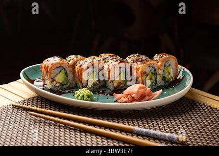 Panini di sushi con salmone, avocado e formaggio spalmabile, conditi con semi di sesamo e salsa di soia, serviti su un piatto con wasabi e zenzero sottaceto Foto Stock