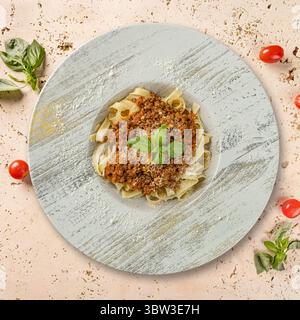 Gustose tagliatelle con salsa alla bolognese, parmigiano e foglie di basilico, creando una perfetta scena culinaria Foto Stock