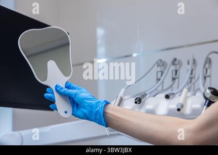 Reflection of Dental Care: Un primo piano sullo specchio di un dentista in un ambiente clinico moderno con strumenti dentali essenziali sullo sfondo Foto Stock