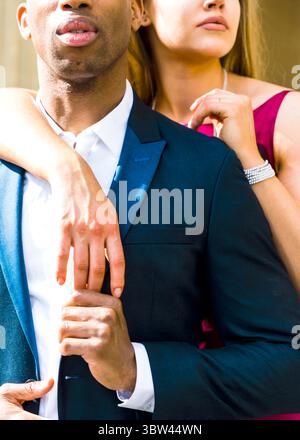 Un uomo con un abito è abbracciato da una donna che indossa un abito rosa. Foto Stock