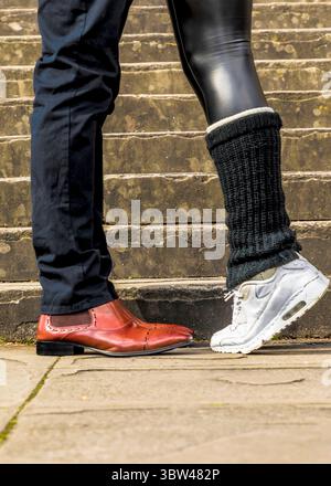 Un uomo con scarpe da passeggio si trova accanto a una persona che indossa scarpe da ginnastica e scalda gambe. Foto Stock