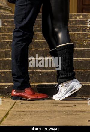 Un uomo con scarpe in pelle rossa si trova accanto a una persona che indossa scarpe da ginnastica bianche e leggings neri. Foto Stock