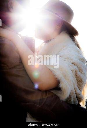 Una coppia si sta abbracciando, con la donna che indossa un cappello e uno scialle di pelliccia. Il sole splende brillantemente dietro di loro. Foto Stock