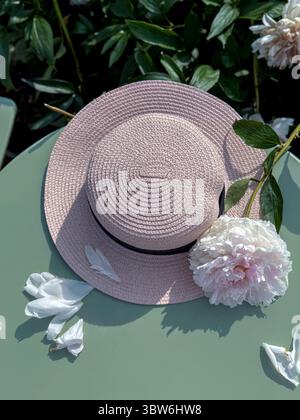 Cappello di paglia in stile vintage su un tavolo di legno tra peonie in fiore. Foto Stock
