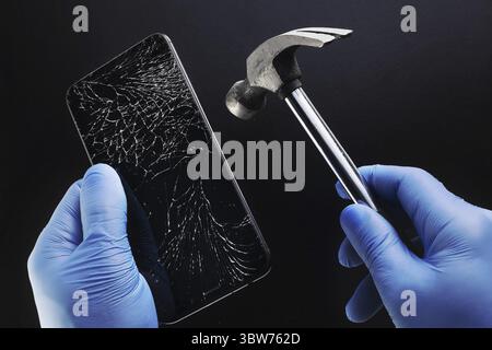 Riparare il telefono. Uno smartphone con un display incrinato e un martello nelle mani di un maestro. Sfondo Foto Stock