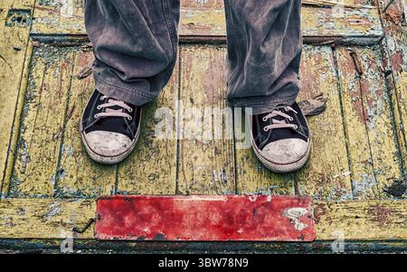 Gambe di un uomo con vecchie scarpe sporche su un pavimento di legno giallo da vicino Foto Stock