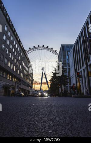 Splendida foto dal basso angolo del London Eye, circondata da edifici della città e da cieli illuminati al tramonto Foto Stock