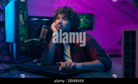 L'indiano arabo annoiato uomo assonnato sbadigliando giocando a tipire il computer maschio prende le cuffie parlando rispondere giocatore stanco affaticato streamer tardi Foto Stock