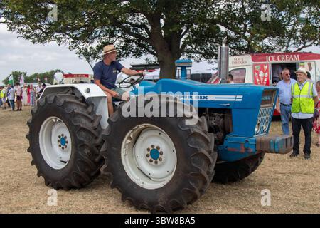 Un trattore Blue County 1164 Super Six guidato da un uomo con cappello in una giornata di sole ad una fiera campestre Foto Stock
