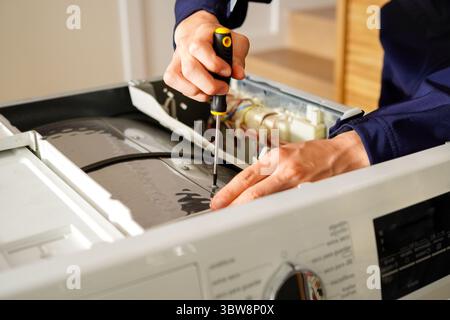Un tecnico addetto alla riparazione di una lavatrice rotta Foto Stock